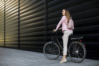 Pretty young woman riding an electric bicycle in urban environment