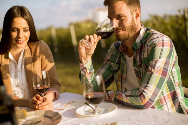 一个英俊的年轻人坐在桌旁 日落时在葡萄园里喝着红酒 — 图库照片
