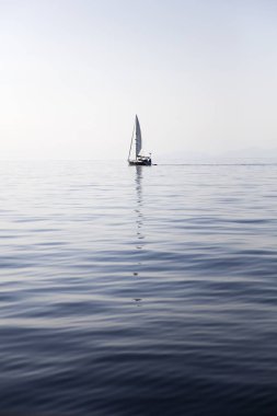 Sakin bir deniz yüzeyinde, suda yansıyan bir tekneyle.