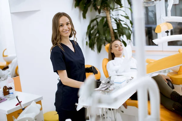 魅力的な若い女性歯科医は彼女のオフィスに立っています 椅子に女性のパティンで — ストック写真
