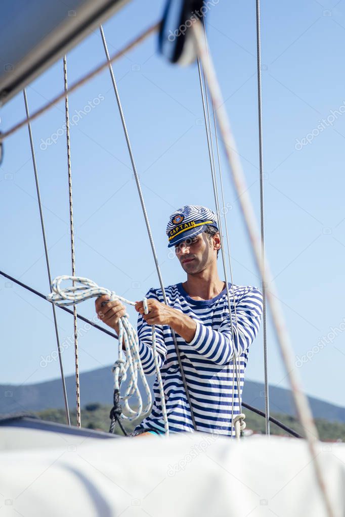 Handsome young man with captain cap on a sailboat at sea on a suuny day
