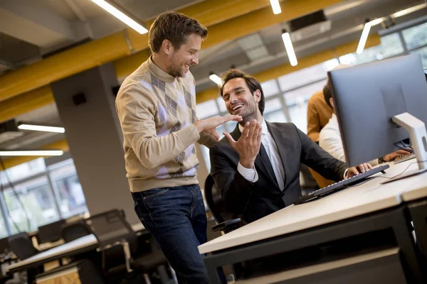 Happy young businessmen handshaking by the table in the office — Stock Photo, Image