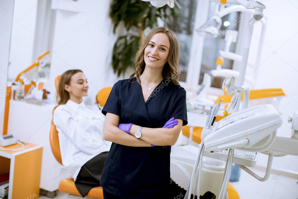 Attractive young female dentist doctor standing in her office, looking at the camera