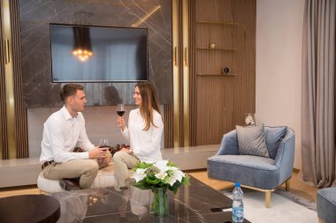 Genç çift, lüks oturma odasında bir kadeh kırmızı şarapla romantik bir akşam geçiriyorlar.