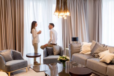 Genç çift, modern dairenin lüks odasında kahve fincanlarıyla gevşeyip sohbet ediyorlar.