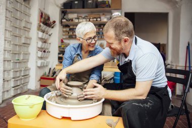 Çömlekçilik sınıfındaki bir öğretmenin yardımıyla çamurda dönen yaşlı bir kadın.