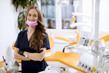 Çekici genç dişçi kadın doktor ofisinde durmuş kameraya bakıyor.