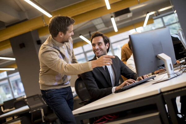 Happy young businessmen handshaking by the table in the modern office