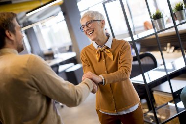 Grateful senior  businesswoman  boss lady hold hand of best employee,  shake hands warm welcoming standing in coworking space clipart