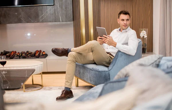 Przystojny Młody Człowiek Siedzi Używa Tabletu Cyfrowego Luksusowym Apartamencie — Zdjęcie stockowe