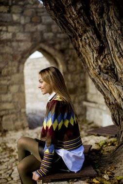 Pretty young woman sitting on the bench watching yellow leaves tree in the autumn park