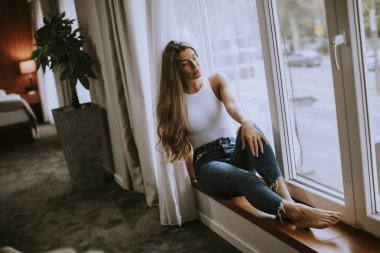 Güzel genç bir kadın, pencerenin kenarında oturuyor.