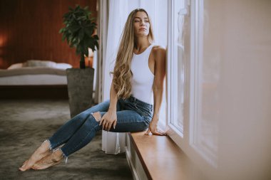 Güzel genç bir kadın, pencerenin kenarında oturuyor.