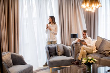 Genç çift kahve içiyor ve lüks dairede dijital tablet kullanıyor.