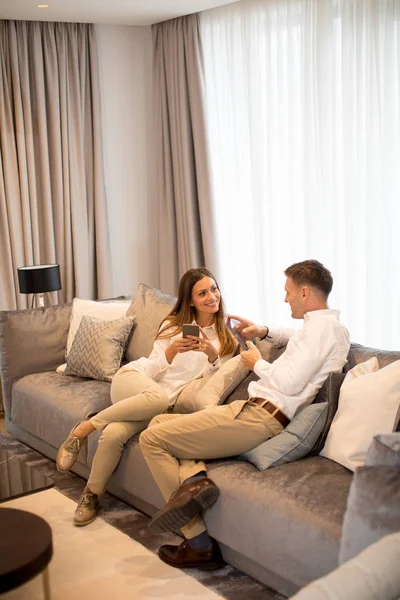 年轻夫妇在豪华客厅的沙发上休息 还使用手机 — 图库照片