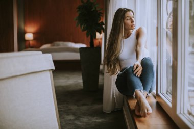 Güzel genç bir kadın, pencerenin kenarında oturuyor.