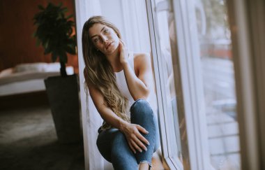Güzel genç bir kadın, pencerenin kenarında oturuyor.
