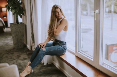 Güzel genç bir kadın, pencerenin kenarında oturuyor.