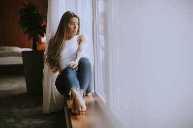 Güzel genç bir kadın, pencerenin kenarında oturuyor.