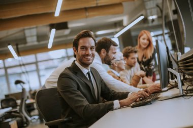 Bir grup genç iş adamı ofiste masaüstü bilgisayarıyla birlikte çalışıyor.