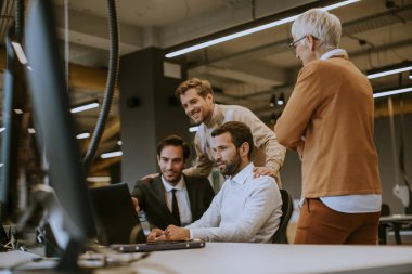 Genç yetişkinler ve kıdemli bayan meslektaşlarıyla birlikte bir grup iş adamı modern parlak ofis içlerinde toplanıyorlar.