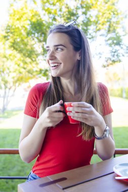 Güneşli bir günde dışarıda kahve içen güzel genç bir kadın.