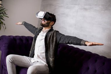 Modern odada sanal gerçeklik gözlüğü takan yakışıklı sakallı genç adam.