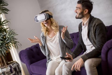 Young couple sitting in the room while young woman wearing a virtual reality glasses