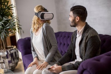 Young couple sitting in the room while young woman wearing a virtual reality glasses