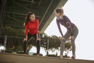 Two pretty young women doing gymnastic exercises outdoor in urban enviroment