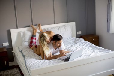 Intimate young lovers using laptop while lying on the bed in the bedroom