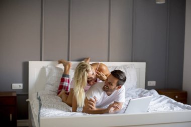 Intimate young lovers using laptop while lying on the bed in the bedroom