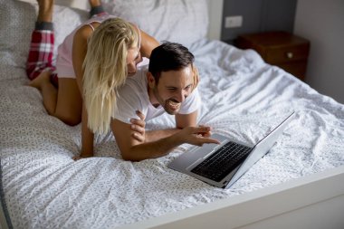 Intimate young lovers using laptop while lying on the bed in the bedroom
