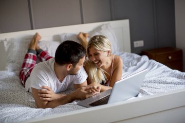 Intimate young lovers using laptop while lying on the bed in the bedroom