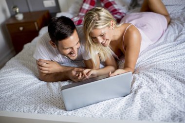 Intimate young lovers using laptop while lying on the bed in the bedroom