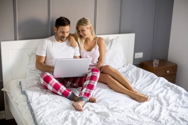 Intimate young lovers using laptop and sitting on the bed in the bedroom