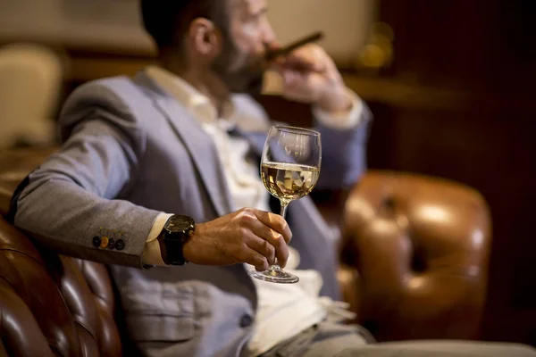 英俊的年轻人品尝着白葡萄酒和吸烟的雪茄 — 图库照片