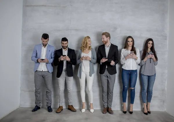 Group of young people with mobile phones standing by the grey wall