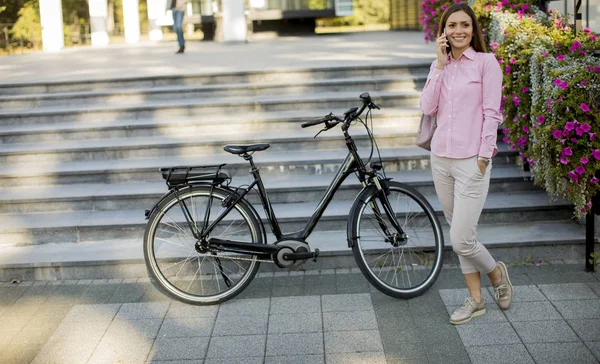 若い女性は自転車の近くに立って スマートフォンの屋外を使用します — ストック写真