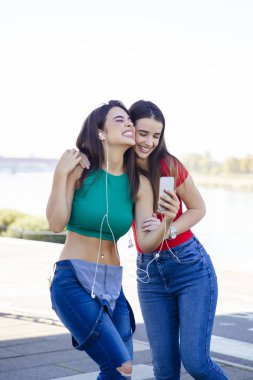 Young pretty  young women stand  and  listening music with earphones using mobile phone at outdoors