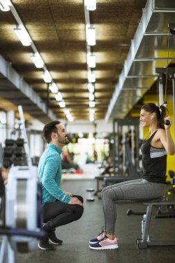 Genç ve güzel bir kadın modern spor salonunda kişisel antrenörle egzersiz yapıyor.
