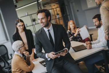 Young businessman using digital tablet in office in front of his team
