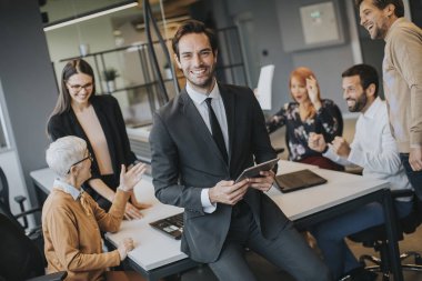 Young businessman using digital tablet in office in front of his team