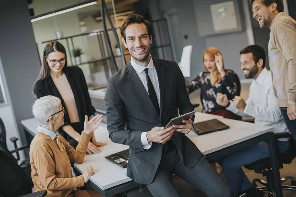 Young businessman using digital tablet in office in front of his team