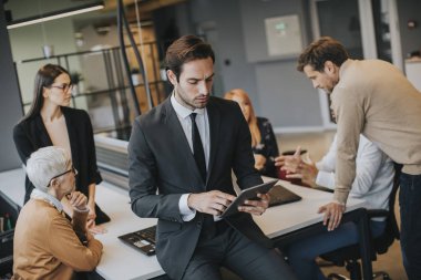 Young businessman using digital tablet in office in front of his team
