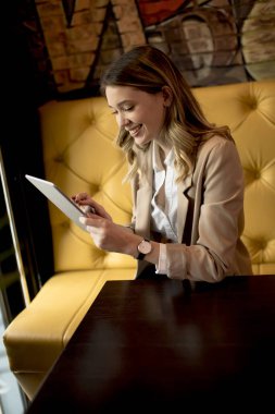 Dijital tabletli gülümseyen genç bayan kafede oturuyor.