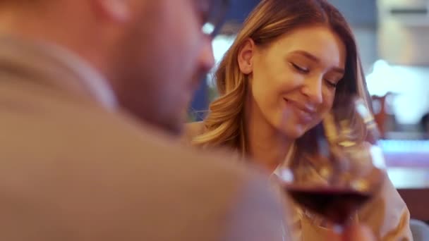 Genç çift restoranda kırmızı şarap kadehleriyle yemek yiyor. — Stok video