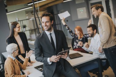 Young businessman using digital tablet in office in front of his team