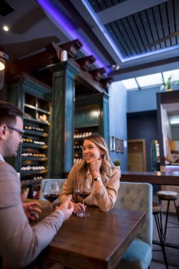 Genç çift restoranda kırmızı şarap kadehleriyle yemek yiyor.