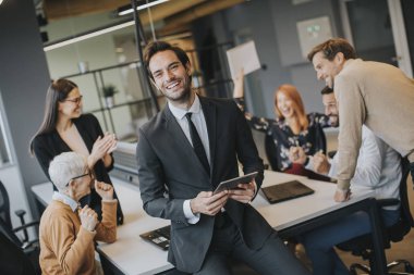 Young businessman using digital tablet in office in front of his team